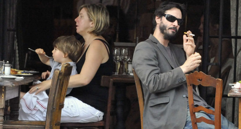 EXCLUSIVE! KEANU REEVES " WITH A CHILD BEHIND HIM "BREAKING THE LAW" AS HE SMOKES HIS CIGARETTE AT "GEMMA RESTAURANT IN THE "BOWERY HOTEL"6/1/2010 IN THE EAST VILLAGE NYC. LOOKING NOT SO CLEAN WITH WINTER BOOTS ON A VERY HOT 90 DEGREE DAY.WITH HIS FEET ACROSS OTHER CHAIR. COPYRIGHTED BY FRANK ROSS 2010 ***NO UNAUTHORIZED USAGE OF THESE COPYRIGHTED PICTURES OR FACE LEGAL ACTION IN A COURT OF LAW" UNLESS MY FEES AND TERMS ARE AGREED TO FIRST BEFORE USAGE. CREDIT:ROSS/FRANK ROSS MEDI