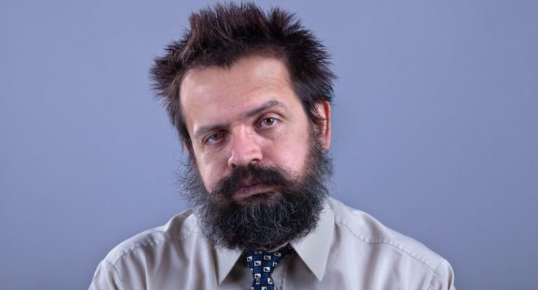 Exhausted man with bushy hair and beard on gray background - copy space