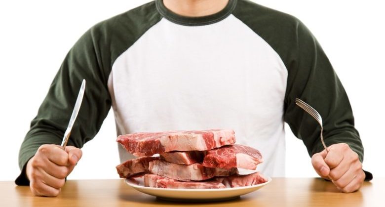 A hungry man holding a knife and a fork ready to eat a stack of raw steak